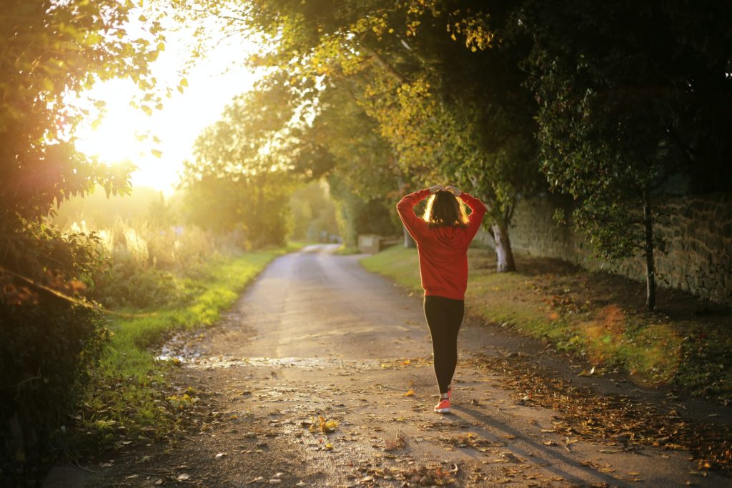A photograph of someone walking down a dirty road on a sunny morning.